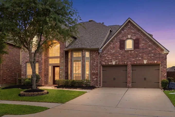 Two-story brick home glowing at dusk on Crested Peak Ln